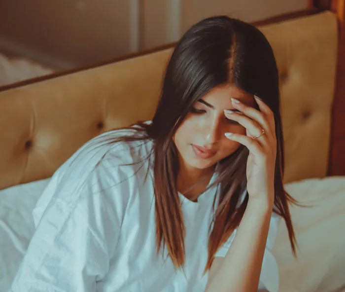 A stressed woman sitting on a bed touching her forehead, overwhelmed by bridezilla stories.