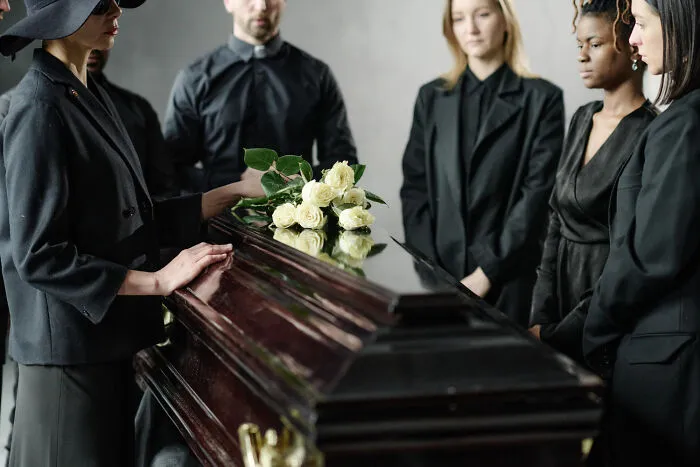 A hand placing flowers on a white casket during a funeral service that went wrong.