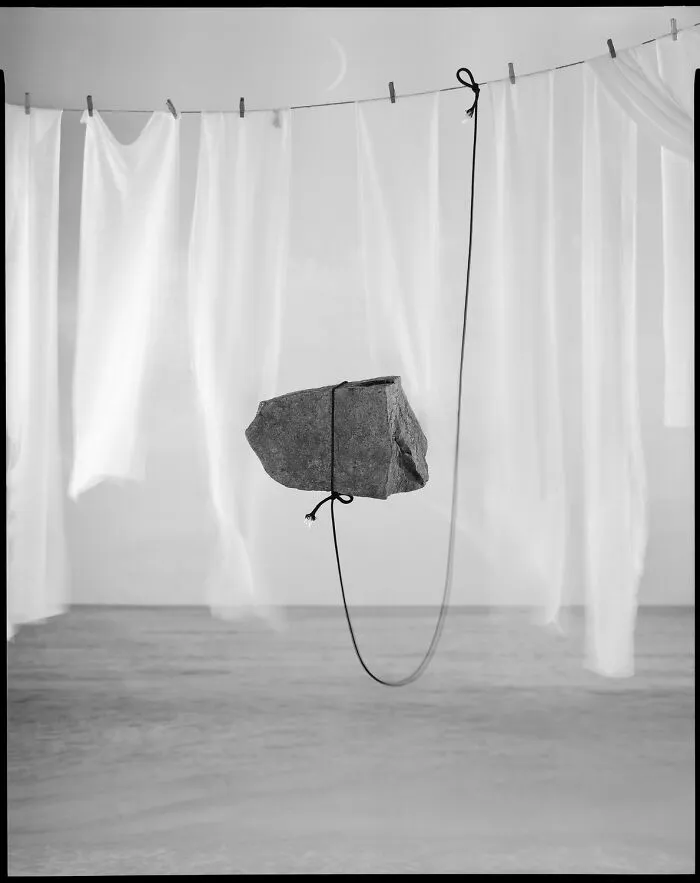 Surreal black-and-white photo of a stone suspended by a string near white drapes from Exposure One Awards.