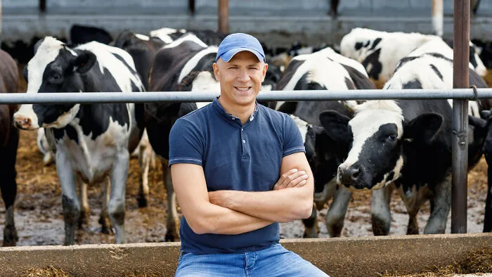 A smiling farmer posing in front of his dairy cows, a story of rural life shared with healthcare workers