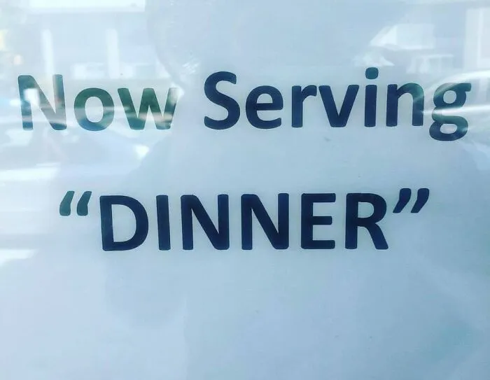 Sign with misused quotation marks reading Now Serving Dinner