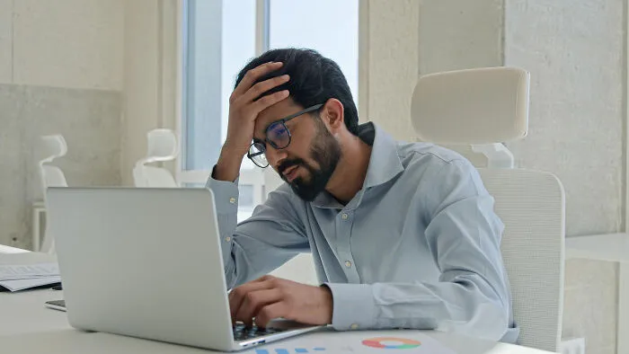 An overwhelmed office worker holding his head, showcasing people share breaking point moments.