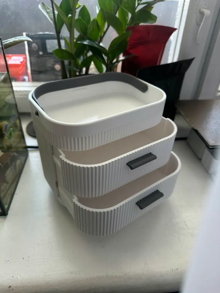 A white 3D prints mini organizer with small drawers next to a plant.