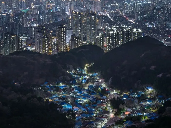 Aerial night landscape showing illuminated city buildings and a glowing village, from the Siena Drone Photo Awards.