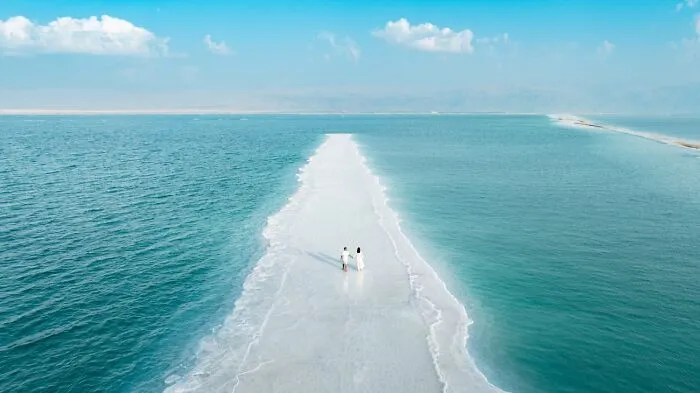 Top-down view of a couple walking along a white sandbar surrounded by turquoise water, from Siena Drone Photo Awards.