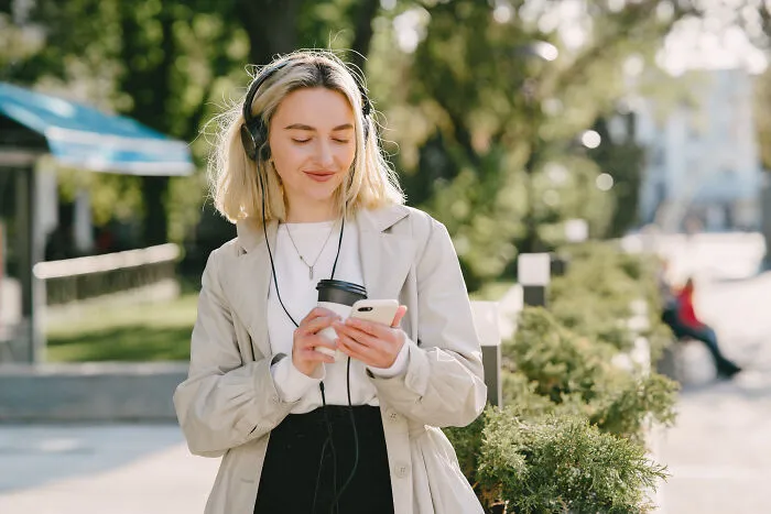 Woman listening to music outdoors with coffee and phone in hand