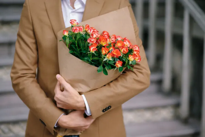 A well-dressed man holding a bouquet of orange roses while considering whether to skip a second date.