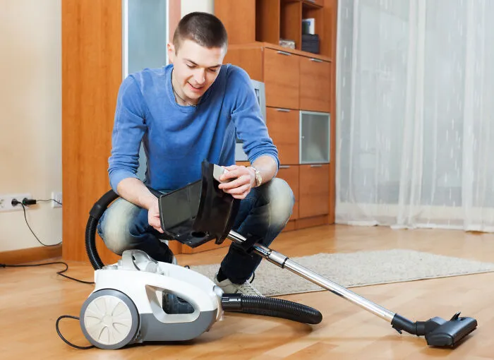 A man emptying a vacuum cleaner canister on the floor, illustrating obvious lies about fixing appliances