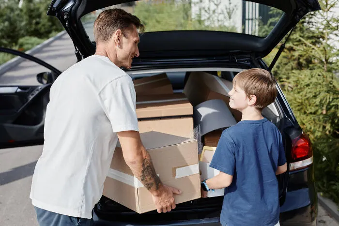 A father and son loading boxes into a car, showing a new start after lifelong friendships changed.