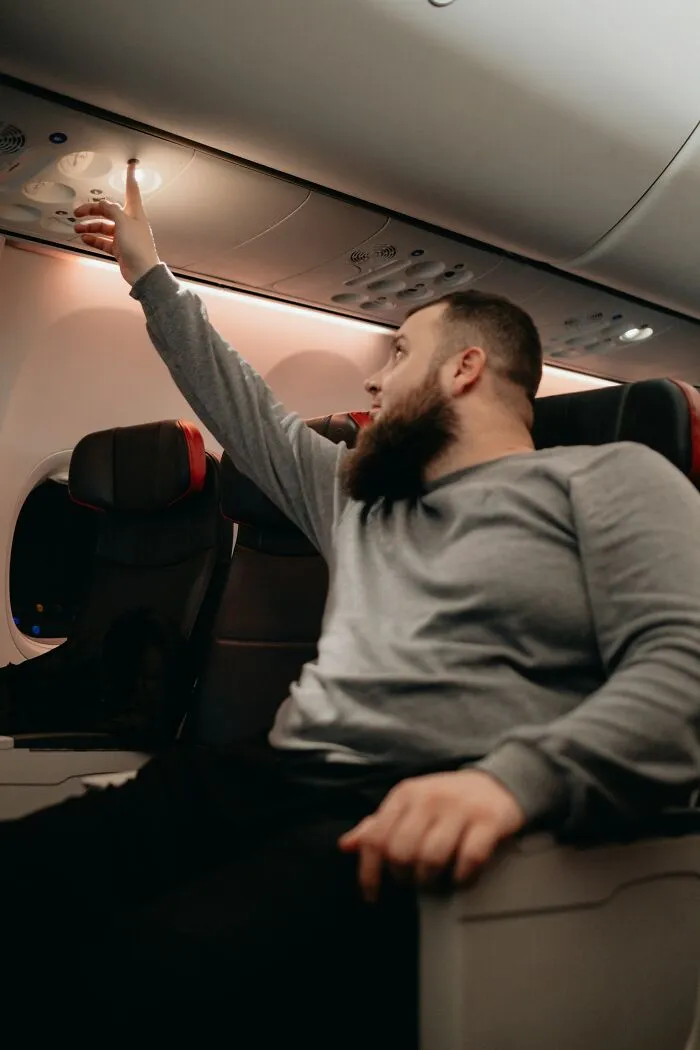 A man reaching up to adjust the overhead light in his seat on flights.