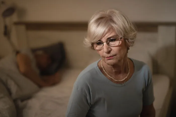 Worried senior woman sitting on a bed representing being disowned by their families
