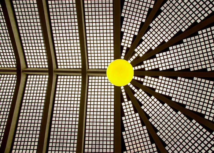 A glowing yellow light under a geometric glass ceiling highlighting the hidden beauty of buildings