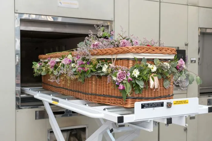 Decorated wicker coffin with flowers on mortuary trolley