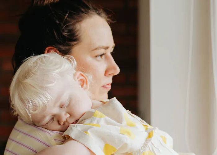 A tired mother embracing her sleeping toddler during early new motherhood