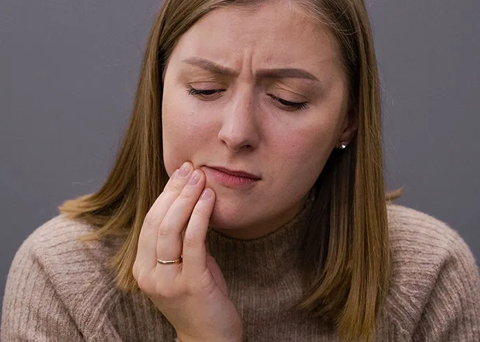 A woman holding her jaw in discomfort, reflecting physical challenges during new motherhood.