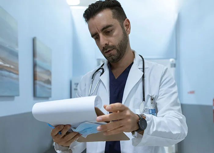 A male doctor reviewing medical charts in a hospital hallway during post-giving birth care.