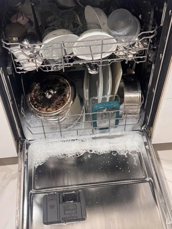 A dishwasher overflowing with soap suds and a burned pot inside, showcasing things went wrong pics.