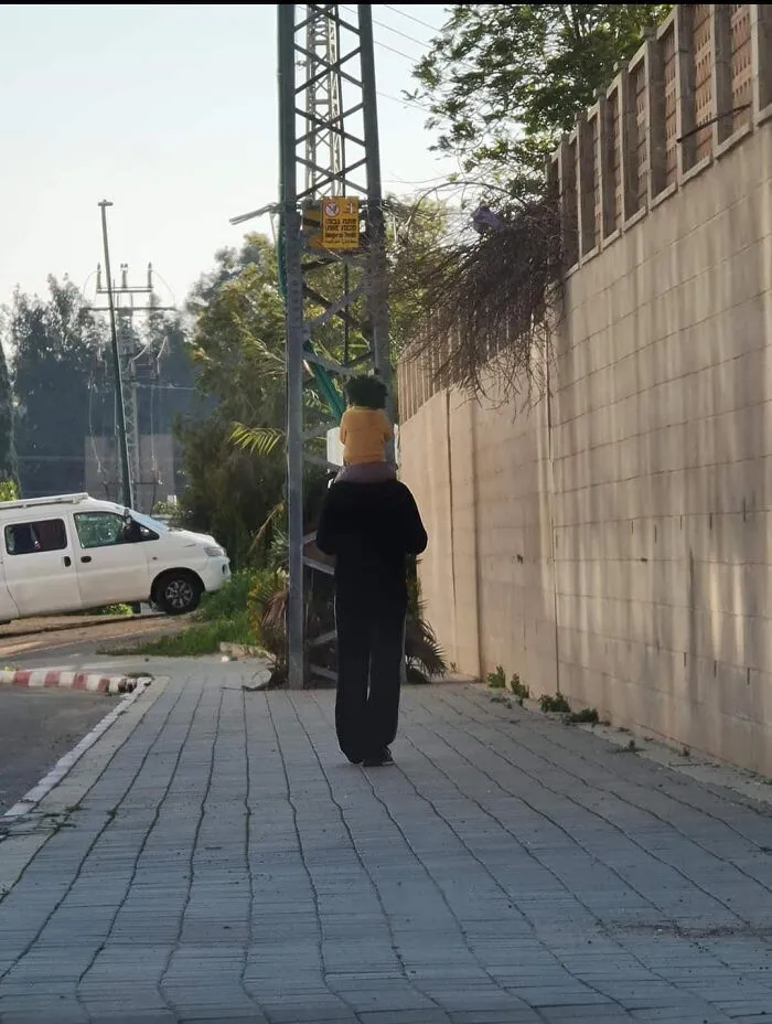 Person walking down a sidewalk carrying a child, creating a perfectly confusing perspective.