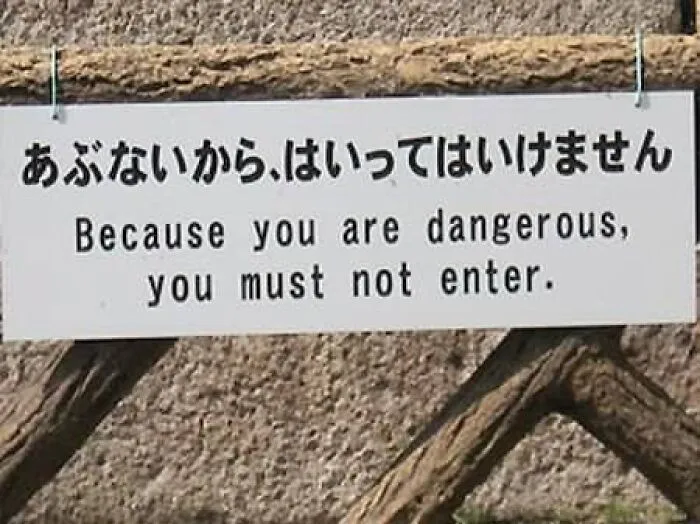 A sign on a wooden fence displaying translation fails saying Because you are dangerous, you must not enter.