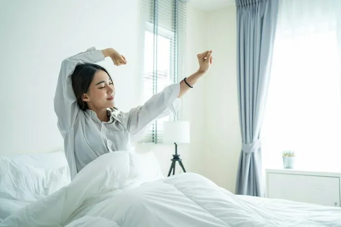 A woman stretching in bed, waking up safely from the scariest true stories.