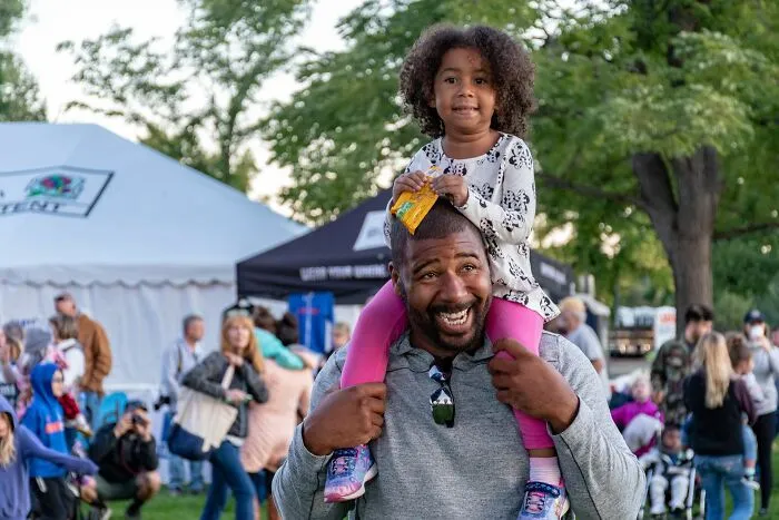 A smiling father carries his young daughter on his shoulders at an outdoor event, inspiring scariest true stories