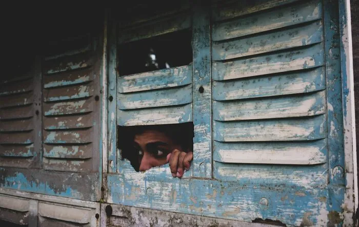 A person peeking through broken wooden shutters, a moment from scariest true stories.