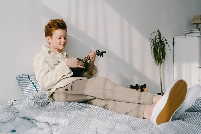 A young boy lying on a bed playing a small ukulele, reminiscent of innocent characters in scariest true stories