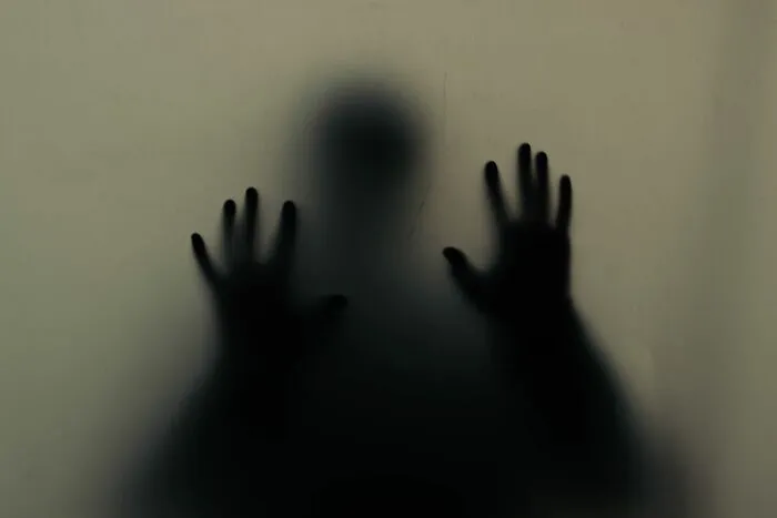 A shadowy silhouette pressing hands against frosted glass, a scene from scariest true stories.