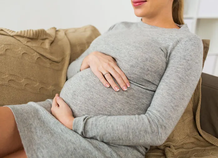 A pregnant woman resting her hands on her stomach, complementing quick-fire jokes.