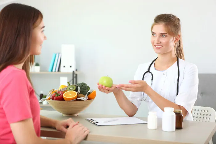 Nutritionist giving an apple to a patient, exchanging quick-fire jokes about healthy eating.