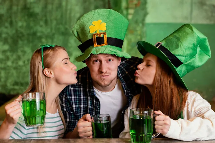 Three friends wearing green hats celebrating with drinks, sharing quick-fire jokes.