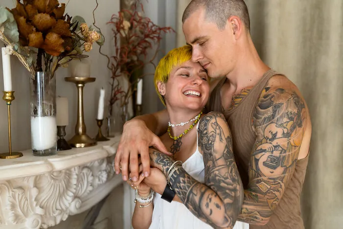 A heavily tattooed couple hugging indoors, illustrating quick-fire jokes.