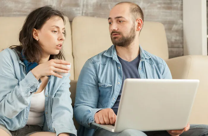 A couple sharing quick-fire jokes while looking at a laptop together indoors.