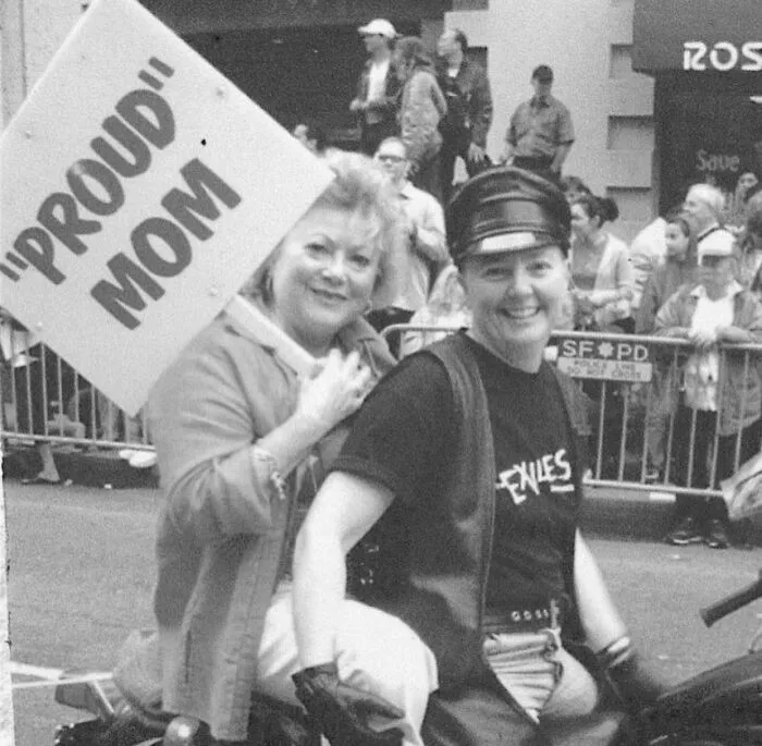 A woman holding a sign with misused quotation marks on the word proud during a parade.