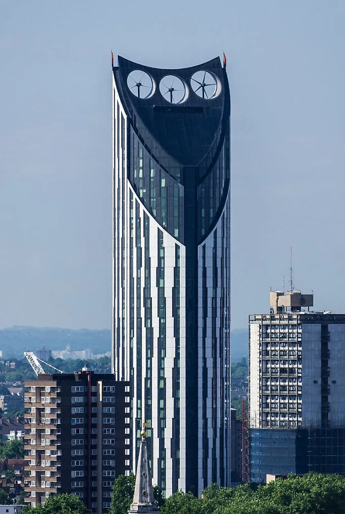 Tall strange building with three large circular wind turbines on top
