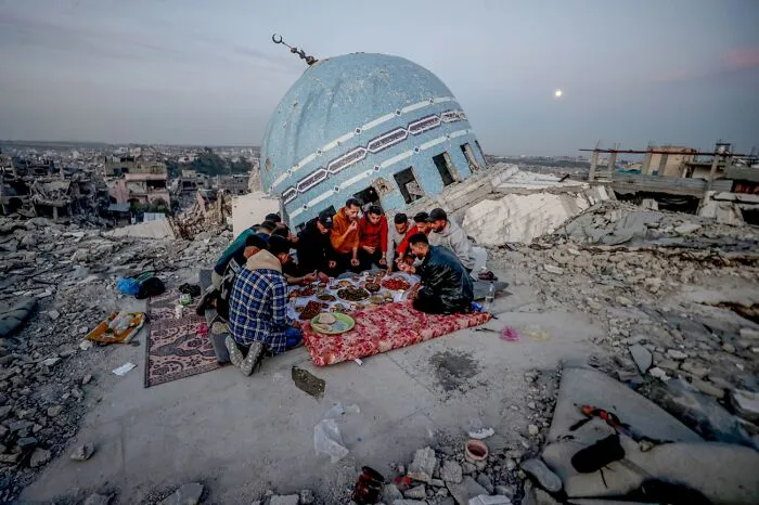 Group of people sharing meal on rubble near damaged mosque dome