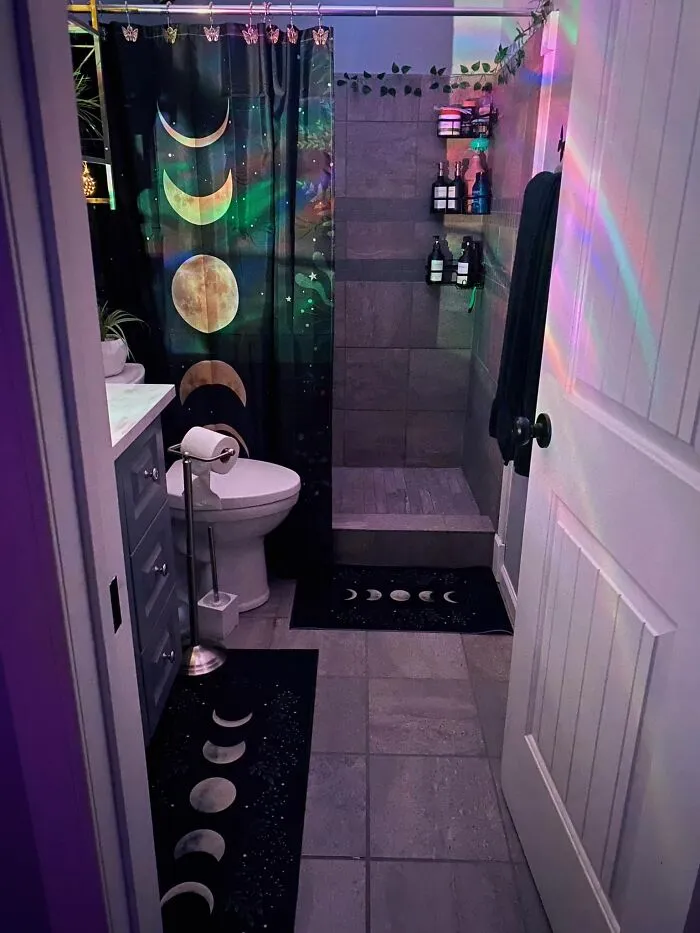 Moody bathroom home makeover featuring moon phase shower curtains, dark tiles, and celestial bath mats.