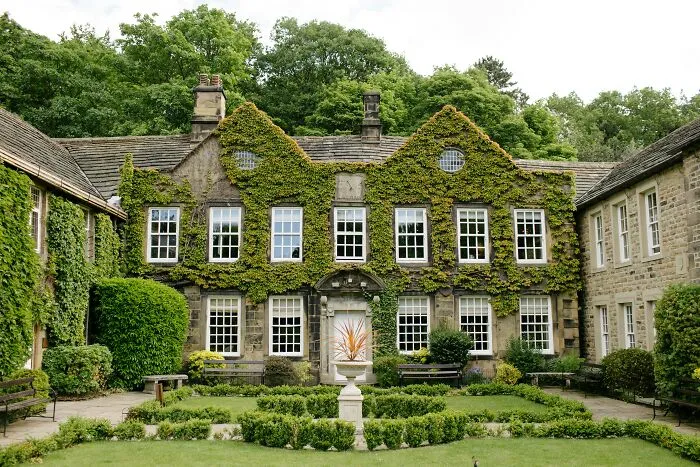 A beautiful English manor house covered in green ivy, showing unethical life pro tips for home curb appeal