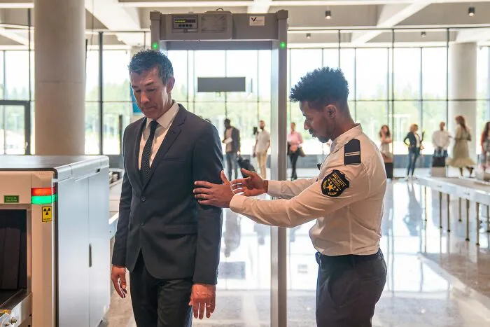 A security guard scans a man at airport security checkpoint, demonstrating unethical life pro tips for travel