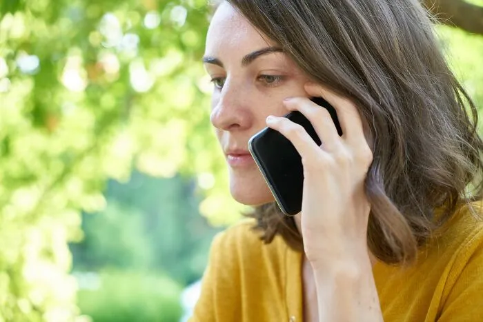 Close-up of a woman talking on a smartphone, on a blurred nature background. Unethical Life Pro Tips.