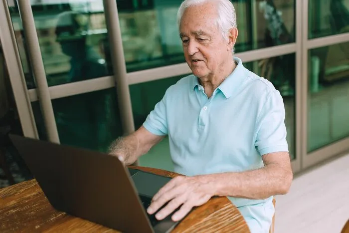 An older man using a laptop, looking up unethical life pro tips to save money online