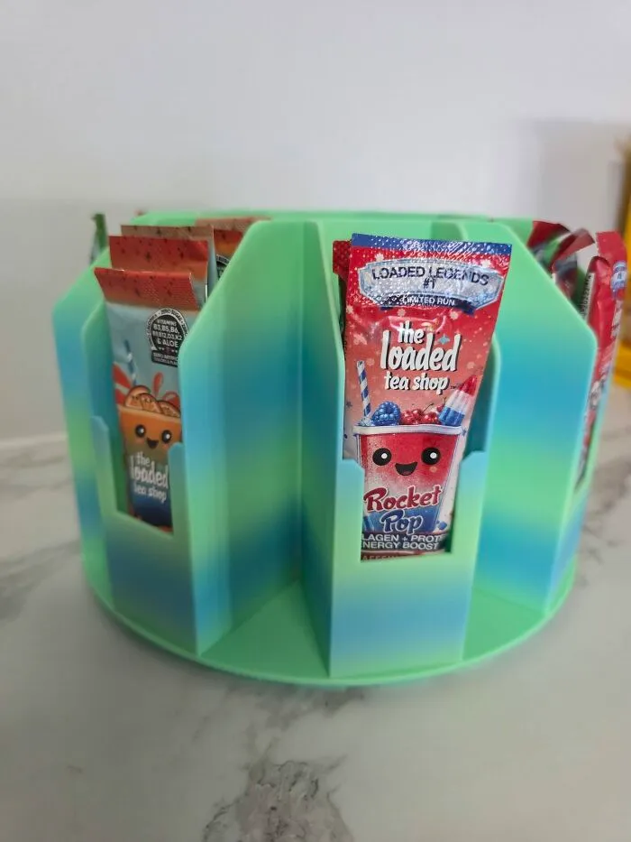A rotating green and blue 3D printer carousel holding tea flavor packets.