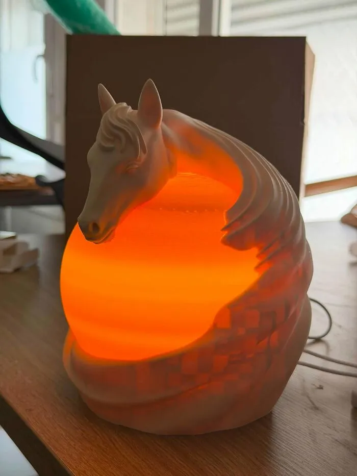 A detailed white horse head lamp printed on a 3D printer glowing with a warm orange light