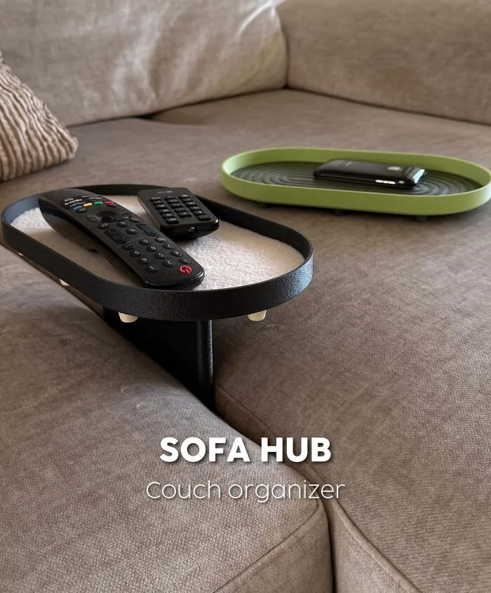 A black 3D printed sofa hub couch organizer holding remote controls on a couch cushion.