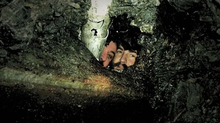 Two faces peering out from a dark hole under a pipe, showcasing entertaining pics.