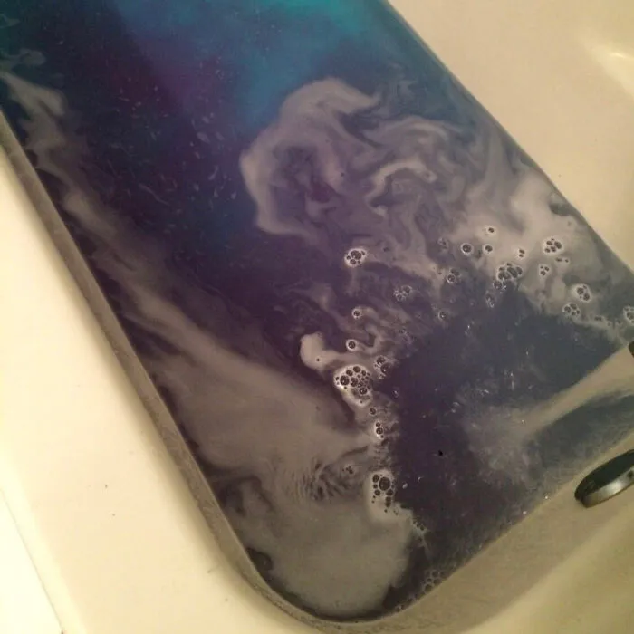 Deep blue soapy bathwater inside a white bathtub creating swirling galaxy patterns in confusing photos.