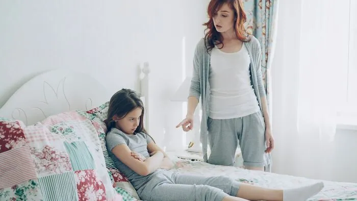 A mother gesturing sternly at her daughter in bed, illustrating dynamic with narcissistic parents.