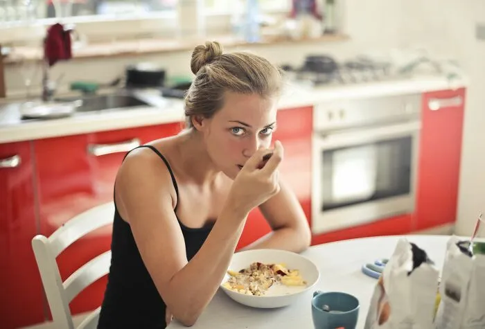 Woman eating breakfast cereal in kitchen about weight-related comments
