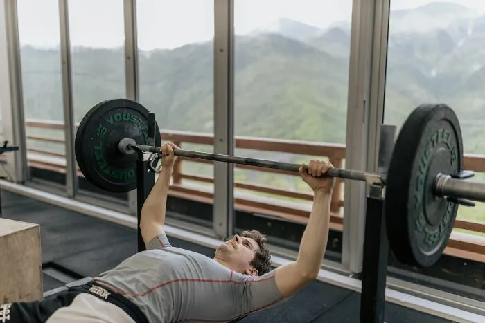 Man lifting heavy barbell bench pressing in gym with mountain view