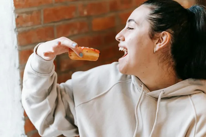 Young woman eating donut indoors near brick wall